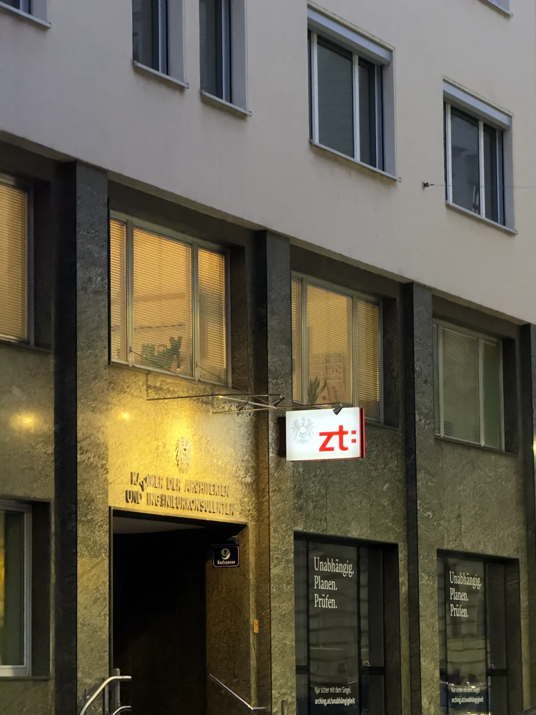 Eingang der Kammer in der Karlsgasse 9 am Abend: Steinportal mit Schriftzug, darüber das beleuchtete zt:-Schild, rechts zwei Schaufenster