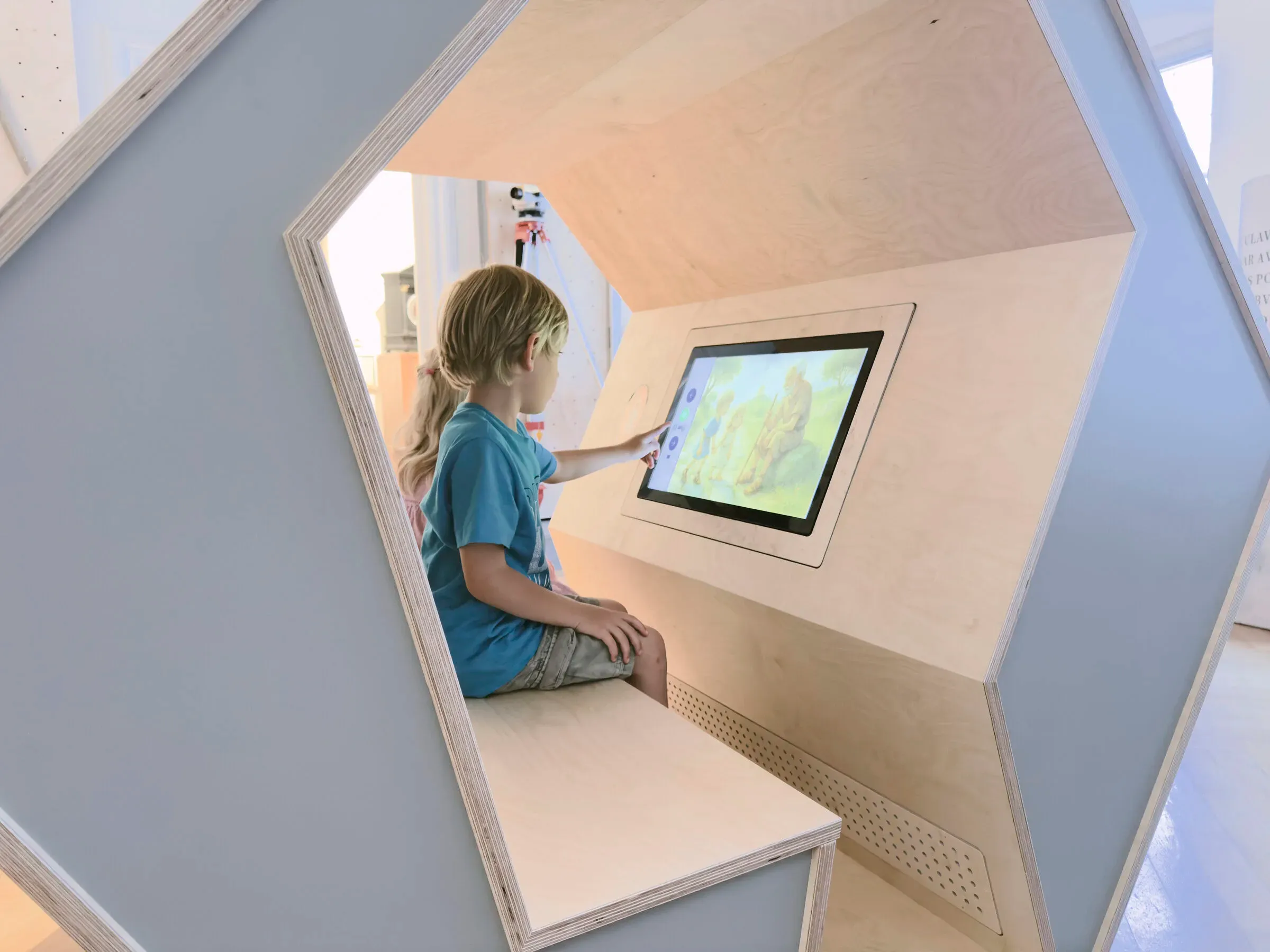 Kind sitzt im Tunnel des Multimediamöbels und bedient einen Touchscreen