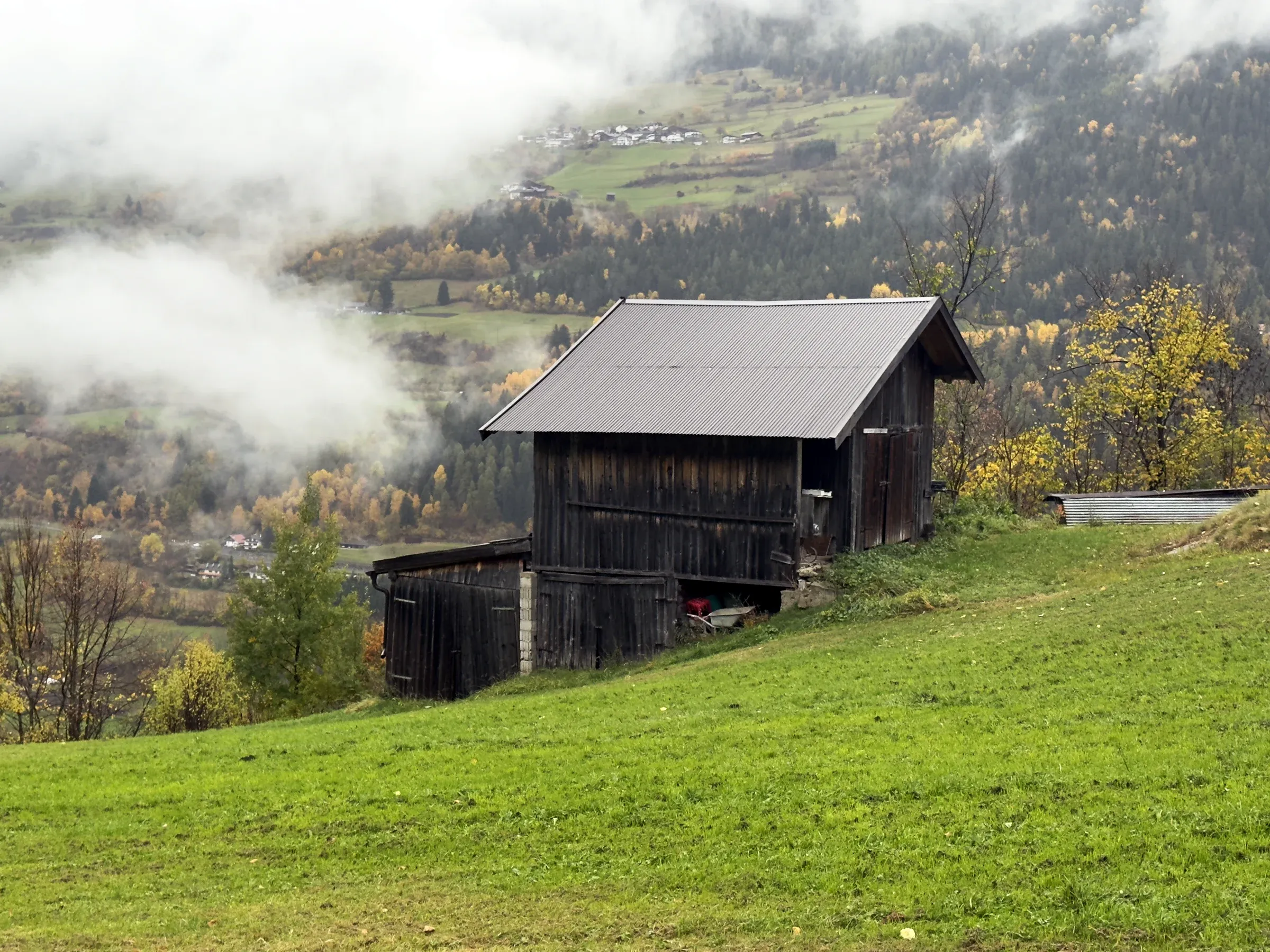 Holzstadel am Hang im Pitztal mit Bretterwänden und Satteldach, dahinter Nebel über dem Tal